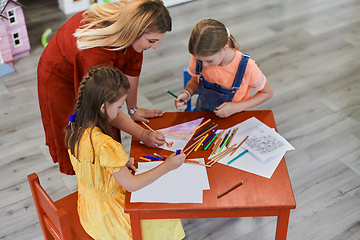 Image showing Creative kids during an art class in a daycare center or elementary school classroom drawing with female teacher.