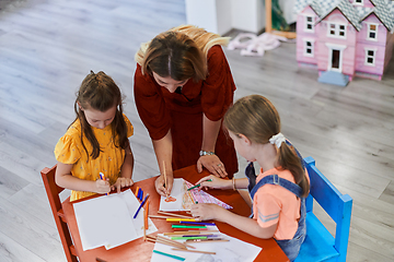 Image showing Creative kids during an art class in a daycare center or elementary school classroom drawing with female teacher.