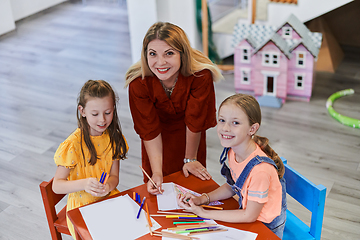 Image showing Creative kids during an art class in a daycare center or elementary school classroom drawing with female teacher.