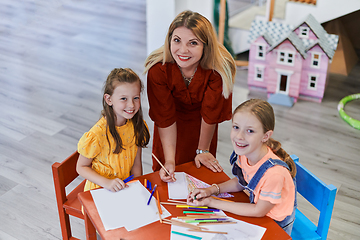 Image showing Creative kids during an art class in a daycare center or elementary school classroom drawing with female teacher.