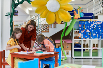 Image showing Creative kids during an art class in a daycare center or elementary school classroom drawing with female teacher.