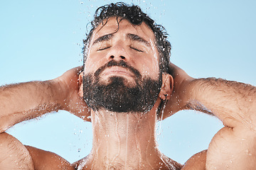 Image showing Face, water splash and man in shower for skincare in studio isolated on a blue background. Dermatology, water drops and male model cleaning, bathing or washing for healthy skin, hygiene and wellness.