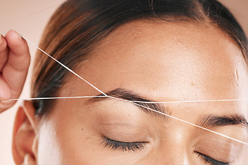 Image showing Eyebrows, grooming and woman threading hair on face for beauty routine, shaping and cosmetics care on a studio background. Zoom, trimming and cosmetic model cleaning facial hair with a thread