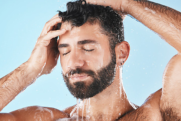 Image showing Face, hair care shower and water splash of man in studio isolated on a blue background. Dermatology, water drops and male model washing, cleaning and bathing for healthy skin, skincare and hygiene.