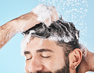 Image showing Face, water splash and man in shower with shampoo in studio on a blue background. Skincare dermatology, water drops and male model cleaning, bathing or washing for hair care, hygiene and wellness.