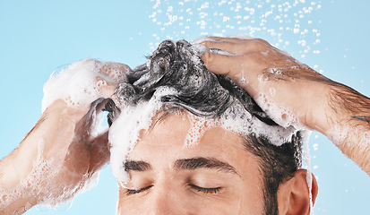 Image showing Face, water splash and shampoo shower of man in studio isolated on a blue background. Water drops, hair care and male model washing, bathing or cleaning for healthy skin, wellness or skincare hygiene