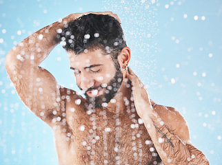 Image showing Water splash, face and man in shower for skincare in studio isolated on a blue background. Water drops, dermatology and male model cleaning, washing or bathing for wellness, healthy skin and hygiene.