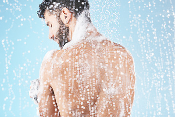 Image showing Shower, water and man with soap for cleaning, washing and hygiene on blue background in studio. Grooming, bathroom and back of male with foam, sponge and water splash for skincare, wellness and spa