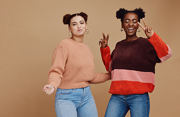 Image showing Peace sign, fashion and women friends in studio with hand gesture, smile and happiness on brown background. Love, friendship and black woman with happy girl for relaxing, cosmetics and emoji together