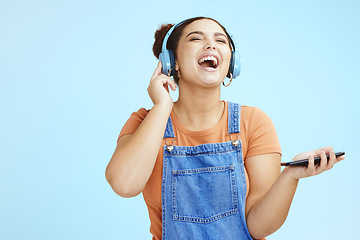 Image showing Mockup, headphones and woman with smartphone, happy or connection on blue studio background. Fun, female or girl laughing, cellphone for music or headset for podcast, online streaming or social media