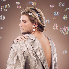 Image showing Beauty, lgbtq fashion and man with bubbles in studio on brown background for cosmetics, style and modern outfit. Creative art, luxury design and non binary model with soap bubbles, jewelry and makeup