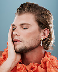 Image showing LGBTQ, fashion and face of queer man with orange clothes, accessories and facial cosmetics on blue background. Transgender, gay or non binary model with beauty makeup, skincare glow or creative style