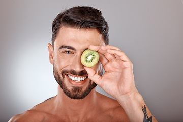 Image showing Man, face and beauty with kiwi, facial care with wellness and organic treatment against studio background. Natural skincare, fruit and eye, wellness mockup with cosmetic care and smile in portrait