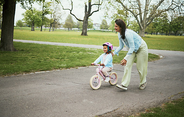 Image showing Kids, bike and a mother teaching her daughter how to cycle in a park while bonding together as a family. Nature, love and children with a girl learning how to ride a bicycle with her mom outside