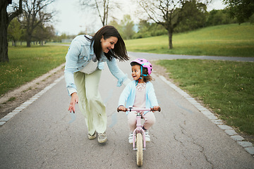 Image showing Children, bike and a mother teaching her girl how to cycle in a park while bonding together as a family. Nature, love and kids with a daughter learning how to ride a bicycle with her mom outside