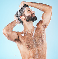 Image showing Haircare, keratin and cleaning with a man in studio on a blue background to take a shower for hygiene. Water, skin and relax with a male washing his hair with shampoo treatment in the bathroom