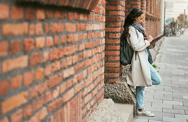 Image showing Woman, student and tablet leaning on brick wall writing, design or doing research in the city. Female university learner or designer working on touchscreen with wireless pen or tech in a urban town