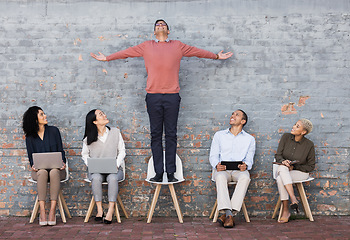 Image showing Business people, waiting room and man standing out for interview, meeting or opportunity against a brick wall. Group of employee workers or interns with technology looking at candidate on chair