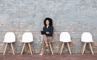 Image showing Job search, tablet and black woman in waiting room on brick wall for career opportunity, hr website and internship. Happy person in chair reading hiring email, Human Resources application and faq