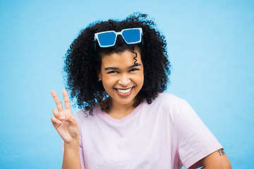 Image showing Portrait, black woman and sign for peace, fashion and casual outfit with girl on blue studio background. African American female, confident lady or gesture with sunglasses, happiness and on backdrop