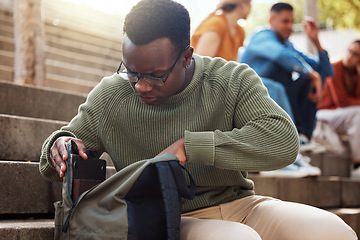 Image showing University, student and black man looking in bag at campus for learning, studying or lost knowledge book. College steps, scholarship and male checking or searching backpack for missing item outdoors.