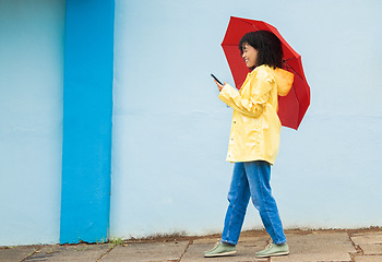 Image showing Woman, raincoat and phone typing with umbrella on city street for social media, internet or urban communication. Smile, happy and walking student with mobile technology for weather app check for rain