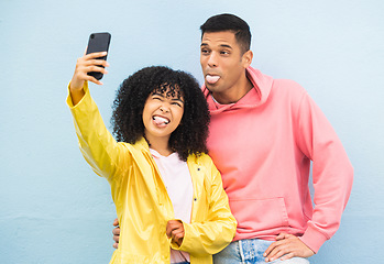 Image showing Happy couple, tongue and phone selfie on isolated blue background for social media, city profile picture and travel vlog. Man, black woman and silly faces bonding for on mobile photography technology