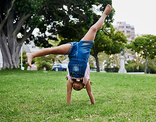 Image showing Cartwheel, child and outdoor park fun of a girl in summer with freedom and happiness. Fun, happy and holiday play of a young kid on green grass in nature on a morning with blue sky and smiling