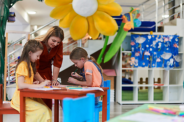 Image showing Creative kids during an art class in a daycare center or elementary school classroom drawing with female teacher.