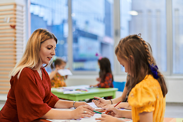 Image showing Creative kids during an art class in a daycare center or elementary school classroom drawing with female teacher.