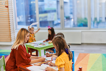 Image showing Creative kids during an art class in a daycare center or elementary school classroom drawing with female teacher.