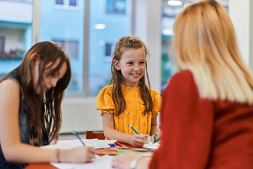 Image showing Creative kids during an art class in a daycare center or elementary school classroom drawing with female teacher.