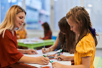 Image showing Creative kids during an art class in a daycare center or elementary school classroom drawing with female teacher.