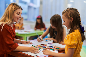 Image showing Creative kids during an art class in a daycare center or elementary school classroom drawing with female teacher.