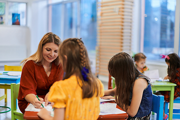 Image showing Creative kids during an art class in a daycare center or elementary school classroom drawing with female teacher.