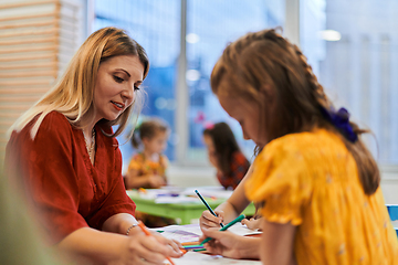 Image showing Creative kids during an art class in a daycare center or elementary school classroom drawing with female teacher.