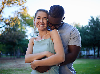 Image showing Happy interracial couple, hug and smile for love, care or bonding together in the nature park. Woman smiling with man hugging her for relationship embrace, support or trust kissing shoulder outside