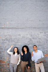 Image showing Business people, peace sign and portrait of friends by a brick wall with a laptop and digital tablet. Happy, smile and corporate team employees standing together with a hand gesture in the urban city