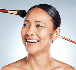 Image showing Makeup, brushes and woman in a studio with a cosmetic, beauty and natural facial routine. Happy, smile and headshot of a mature female with face or skin cosmetics and brush posing by gray background.