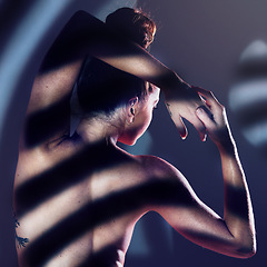 Image showing Back, body and nude with a model woman posing in studio against a dark background with sunlight and shadow. Art, naked and beauty with a young female standing seductively with a sensual pose