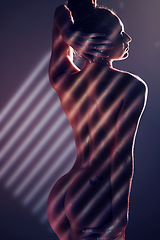 Image showing Sensual, blinds and woman posing in a studio with an alluring, sexy and seductive pose with light. Slim, naked and nude body of a female model with stripe pattern isolated by a dark black background.