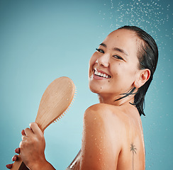 Image showing Beauty, brush and shower by woman in studio for cleaning, hair care and wellness on blue background mockup. Portrait, water splash and asian girl model happy, relax and skincare, hair and face care