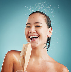 Image showing Portrait, bath brush and woman in a shower for cleaning, wellness and skin exfoliate, beauty and grooming in a studio. Skincare, water splash and face of asian model washing, relax on blue background