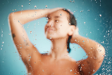 Image showing Glass, shower and hygiene with a woman cleaning or washing her body in studio on a blue background. Water, relax and wellness with a female in the bathroom to clean, wash or hydrate her skin