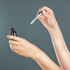 Image showing Skincare, beauty and hands with face serum in a studio for a health, wellness and natural skin routine. Cosmetic, self care and facial oil for a healthy facial treatment isolated by a gray background