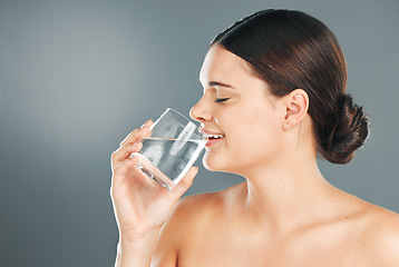 Image showing Woman, glass and drinking water for hydration, skincare or nutrition for sustainability against grey studio background. Happy female with smile in beauty for fresh clean sustainable liquid on mockup