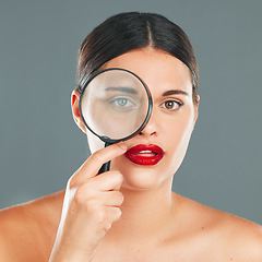 Image showing Portrait, magnifying glass and eye with a model woman in studio on a gray background for beauty or skincare. Face, makeup and search with an attractive young woman checking her skin for cleaning