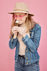 Image showing Young girl, smell flower and smile for modern gen z or millennial fashion, freedom and calm peace in pink background. Happy female, flowers scent and happiness with trendy or edgy clothes in studio