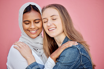 Image showing Hug, happy and women friends in a studio with love, care and bond for friendship or support. Happiness, smile and muslim woman embracing a lady from Australia while isolated by a pink background.