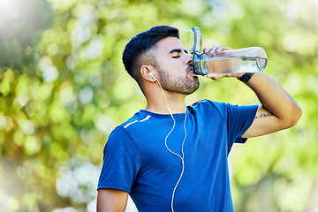 Image showing Nature, running and thirst, a man drinking water on fitness break with headphones in park. Health, exercise and freedom, runner in forest with a drink from bottle while on run in natural landscape.